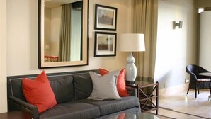 A modern hotel room with a grey sofa, red and grey cushions, a glass coffee table, and two framed pictures on the wall.