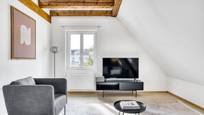 Een moderne woonkamer met een grijze bank, een zwarte entertainmentkast en een flatscreen televisie.
