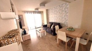 A living room with a sofa, a dining table with chairs, a coffee table, and a patterned wall.