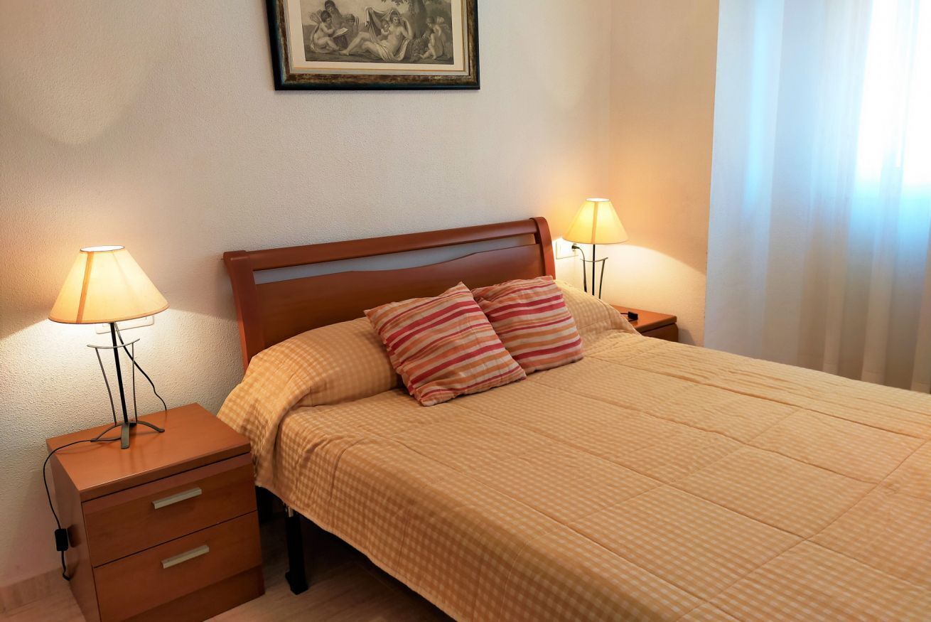 Un letto ben rifatto con cuscini a righe, una testiera in legno e due abat-jour.