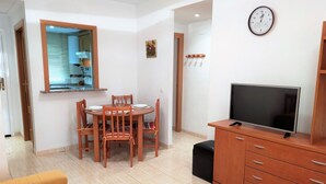 Un comedor con una mesa y sillas de madera, un televisor sobre un mueble de madera, y un reloj en la pared.