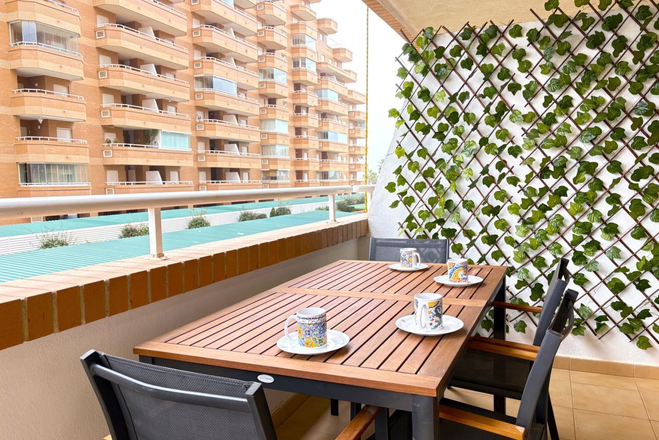 Un balcon avec une table en bois, dressée pour deux personnes, une chaise en métal et un mur recouvert d’une plante grimpante.