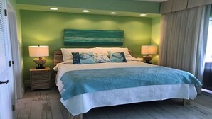 A bedroom with a bed, two bedside tables, a nightstand, a green wall, a painting, and a window with curtains. - Breathtaking view (Rum Point)