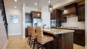 A kitchen with dark wood cabinets, a granite countertop, and a built-in island with wicker bar stools. - Pebble Beach Oasis by RedAwning (Washington)