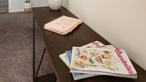 Una habitación con una mesa de madera oscura, un florero blanco con plumas de pluma, un espejo redondo y una libreta.