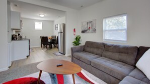 A modern living room with a gray sofa, a wooden coffee table, and a red and gray striped rug. There is a dining area with a table and chairs, and a kitchen area with white cabinets and appliances. - Fabulous Retreat! Centrally located. Quiet & Cozy! Sleeps 4. Hi Sp Wifi & more. (Hanahan)
