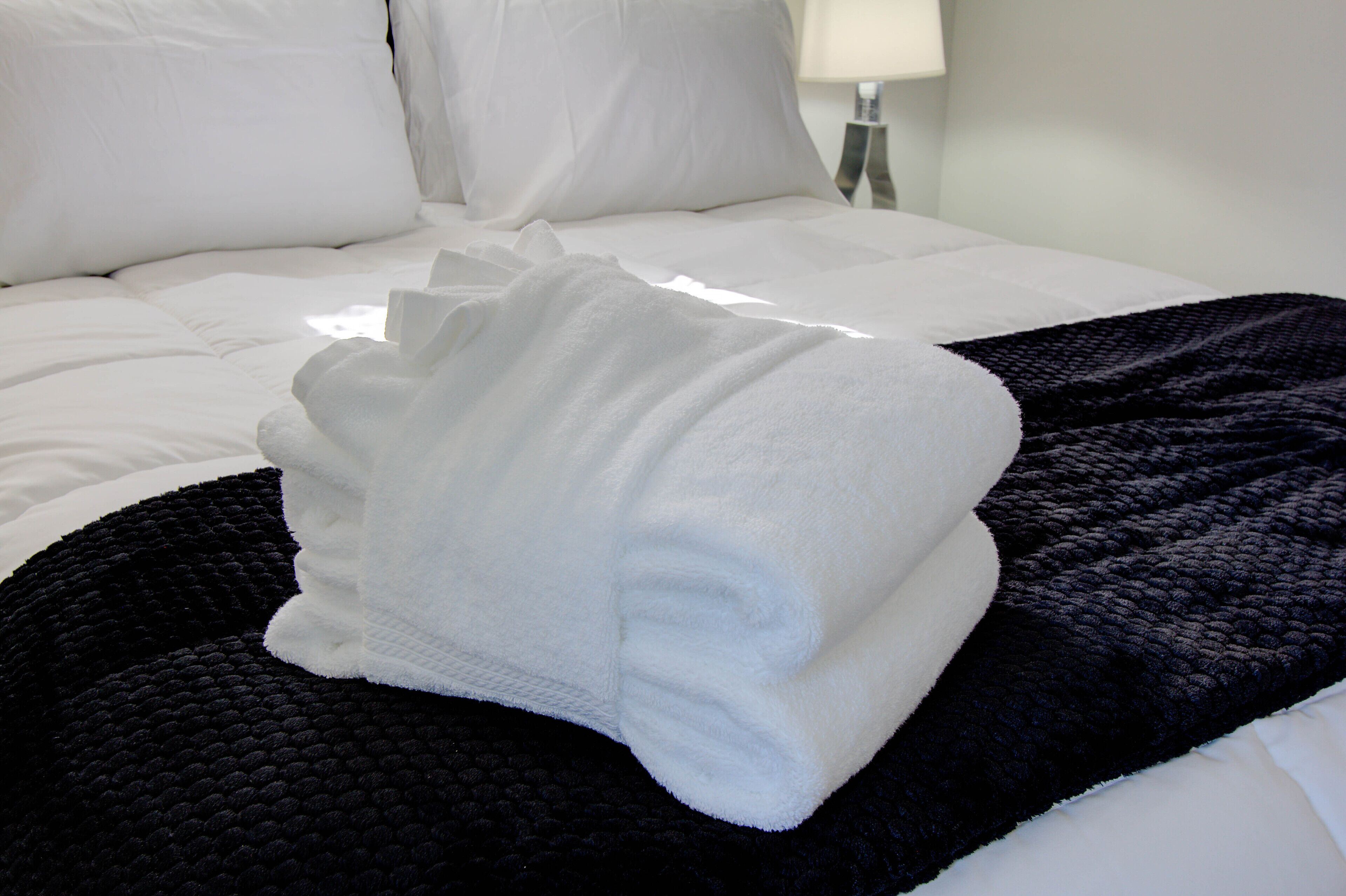A neatly made bed with white linens and a folded white towel on a black textured blanket.
