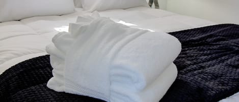 A neatly made bed with white linens and a folded white towel on a black textured blanket.