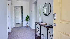 A hallway with a carpeted floor, a potted plant, a console table with a vase, a mirror, and a door with a keypad lock. - Fabulous Retreat! Centrally located. Quiet & Cozy! Sleeps 4. Hi Sp Wifi & more. (Hanahan)
