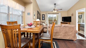 A dining area with a wooden table and chairs, a television in the background, and a ceiling fan. - Stunning Lake View Penthouse - Pool - Close to SDC (Branson)