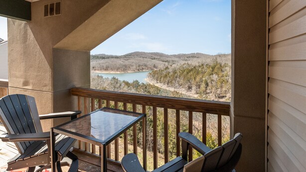 A balcony with a table and chairs, overlooking a river and forested hills. - Stunning Lake View Penthouse - Pool - Close to SDC (Branson)