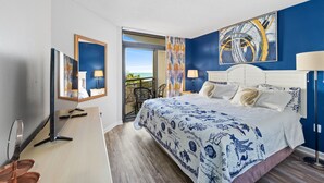 A hotel room with a large bed, a TV, a desk, and a balcony with a view. - Double balcony ocean view condo at Ocean reef resort (Myrtle Beach)