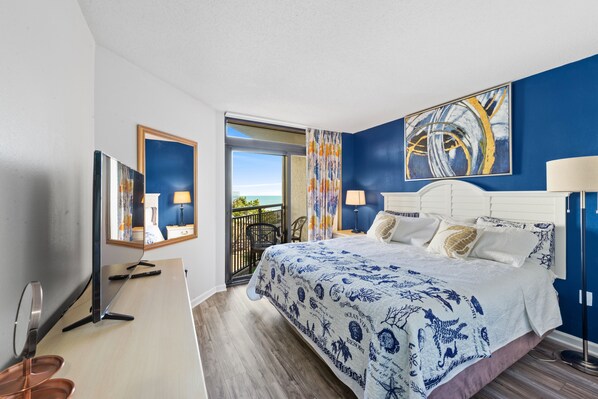 A hotel room with a large bed, a TV, a desk, and a balcony with a view. - Double balcony ocean view condo at Ocean reef resort (Myrtle Beach)