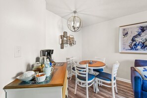 A dining area with a wooden table, white chairs, a coffee machine, and a decorative light fixture. - Double balcony ocean view condo at Ocean reef resort (Myrtle Beach)