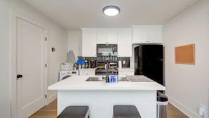 Una cocina moderna con armarios blancos, un lavamanos de acero inoxidable y un refrigerador negro.