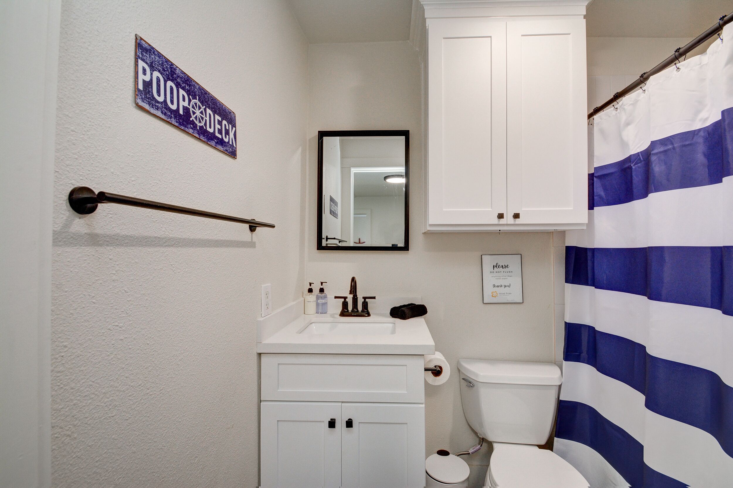 A bathroom with a toilet, sink, mirror, and a sign that reads "POOP DECK".