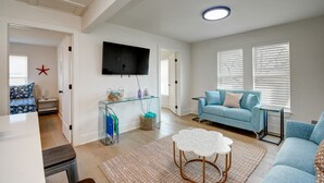 Un salón moderno con un sofá azul, una mesa de centro de vidrio y un televisor de pantalla plana montado en la pared.