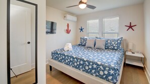 Un dormitorio con cama, ventilador de techo, mesita de noche y ventana con persianas.