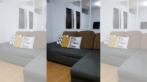 A modern living room with a sectional sofa, a coffee table, and a wooden floor. - 2-Bedroom Condo w/ Unli Wifi, Netflix, Prime Video, Apple TV, Game Console, Pool (Imus)