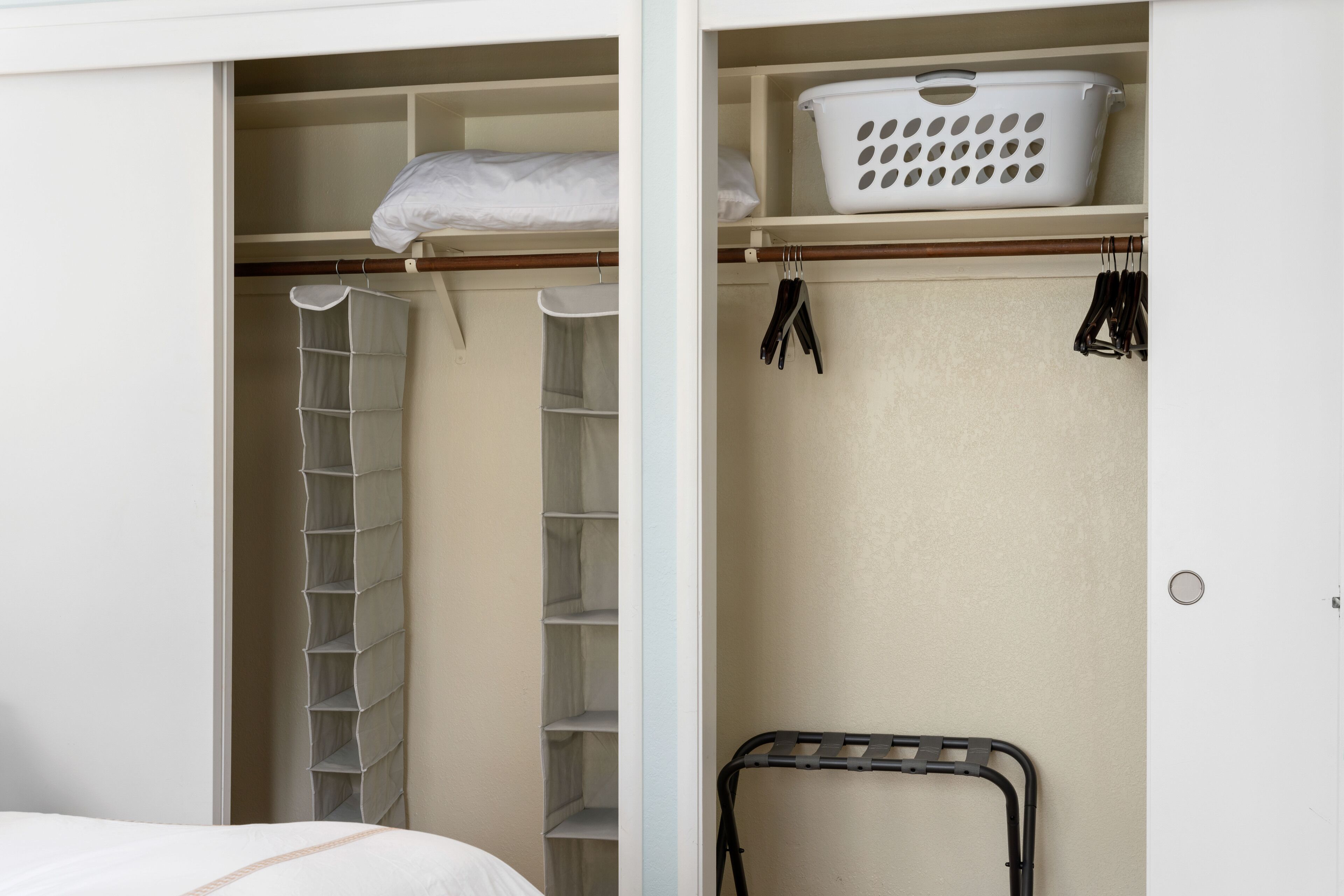 A bedroom with a bed, a closet with shelves, a hanging rack, and a laundry basket.