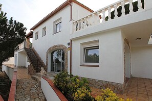 Stunning two-story building with a balcony and stone staircase, set amidst a charming garden with yellow flowers.