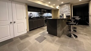 A modern kitchen with dark cabinets, a central island with bar stools, a microwave, and a stone backsplash.