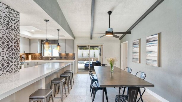 A modern kitchen with a long island, bar stools, pendant lighting, and a ceiling fan.