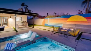 A modern outdoor pool area with lounge chairs, a fire pit, and a colorful wall mural.