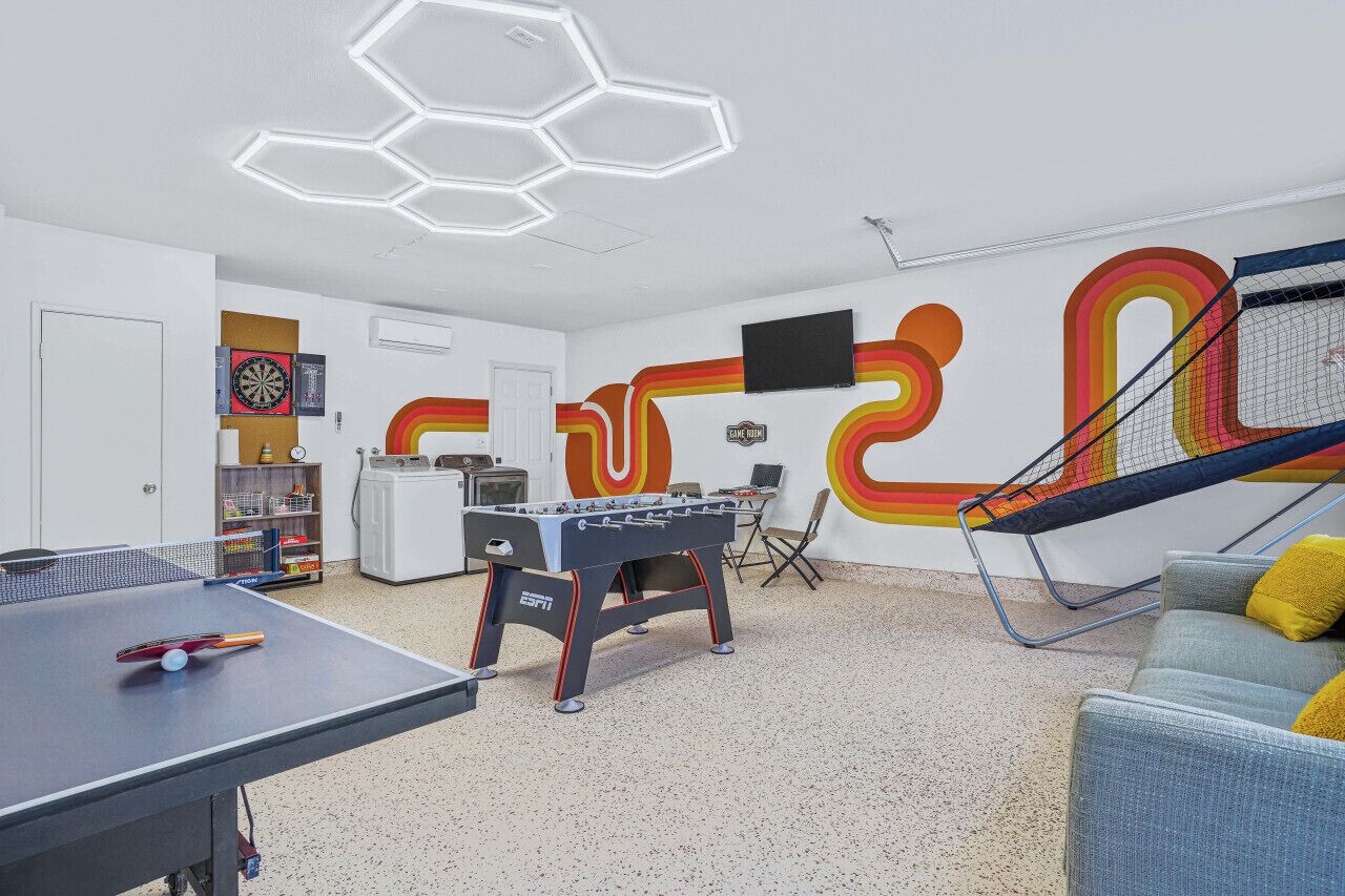 A room with a foosball table, ping pong table, and a TV mounted on the wall.