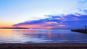 Een strand met een houten steiger die zich uitstrekt over rustig water, waarin de zonsondergang weerspiegelt.