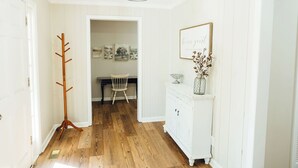 A hallway with wooden flooring, a coat rack, a white cabinet with a vase, and a framed quote on the wall. - NEW HotTub! Spacious cottage convenient to town, wineries & outdoor adventures! (Dahlonega)