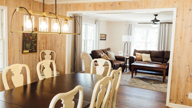 A dining area with a wooden table and chairs, a chandelier, and a living room with a sofa and a coffee table. - NEW HotTub! Spacious cottage convenient to town, wineries & outdoor adventures! (Dahlonega)