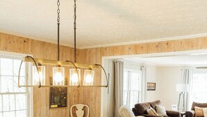 A dining area with a wooden table and white chairs, a chandelier, and a living room with a sofa and lamp. - NEW HotTub! Spacious cottage convenient to town, wineries & outdoor adventures! (Dahlonega)