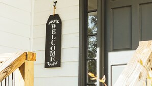 A wooden porch with a 'WELCOME' sign, a dark door, and a light-colored wall. - NEW HotTub! Spacious cottage convenient to town, wineries & outdoor adventures! (Dahlonega)