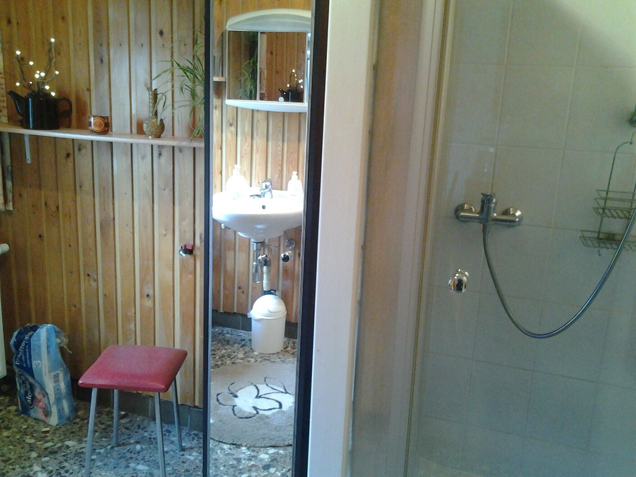 Ein Badezimmer mit Holzvertäfelung, einem Waschbecken, einer Toilette, einer Dusche und einem roten Hocker.