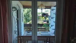 Une pièce dotée d’une porte-fenêtre coulissante donnant sur un patio extérieur avec une table en bois, des chaises et des jardinières suspendues.