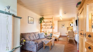 Una sala de estar acogedora con un sofá, una mesita, una estantería y un comedor con una silla.