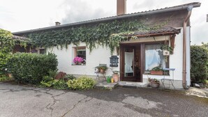 Una casa con porche cubierto, una ventana adornada con planta colgante y una puerta con cortina.