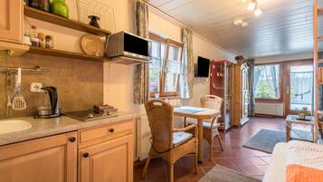 Une cuisine équipée d’un four à micro-ondes, d’une cuisinière et de divers ustensiles de cuisine. On y trouve également un coin repas avec une table et des chaises, ainsi qu’un lit recouvert d’une couverture orange.