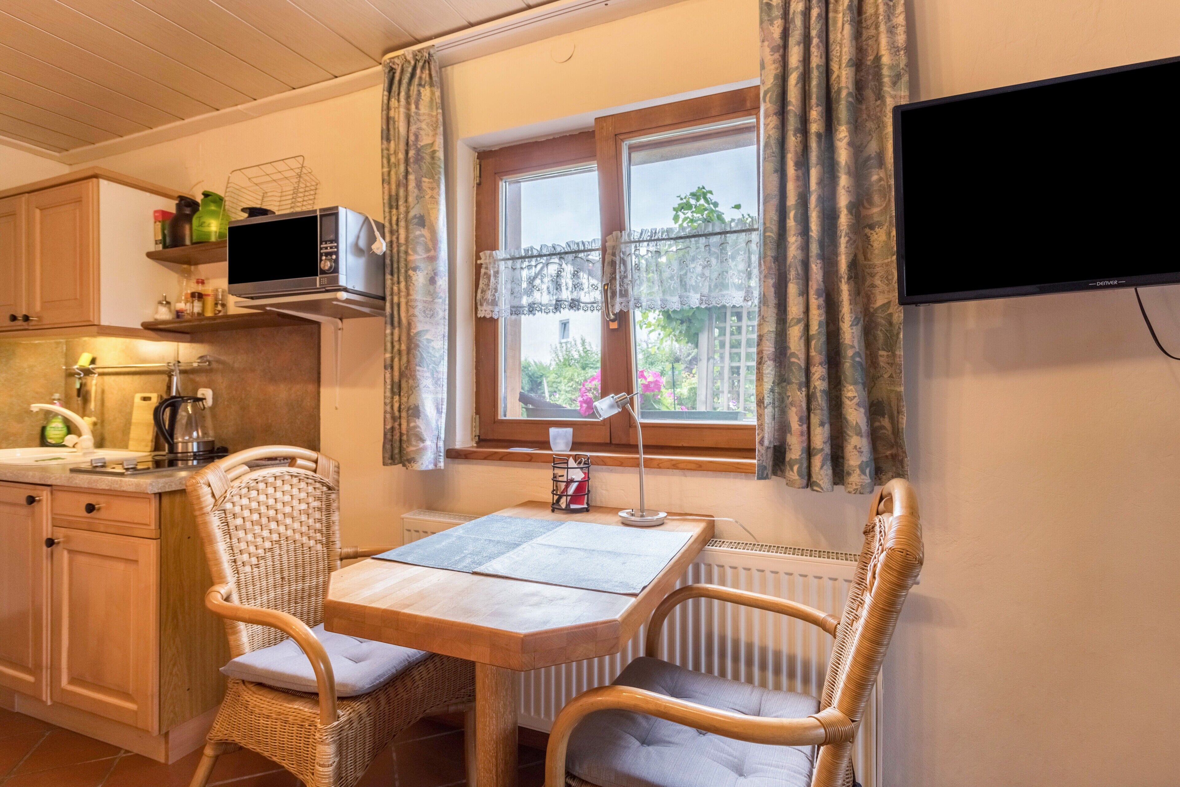 A kitchen with a dining table, wicker chairs, a microwave, and a window with curtains.