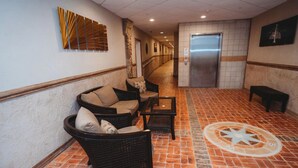 A hallway with wicker furniture, a tiled floor, and a wall-mounted compass. - BEACH LEVEL CONDO L08-2BR/2BA-Private Beach-Indoor Pool. (Geneva-on-the-lake)