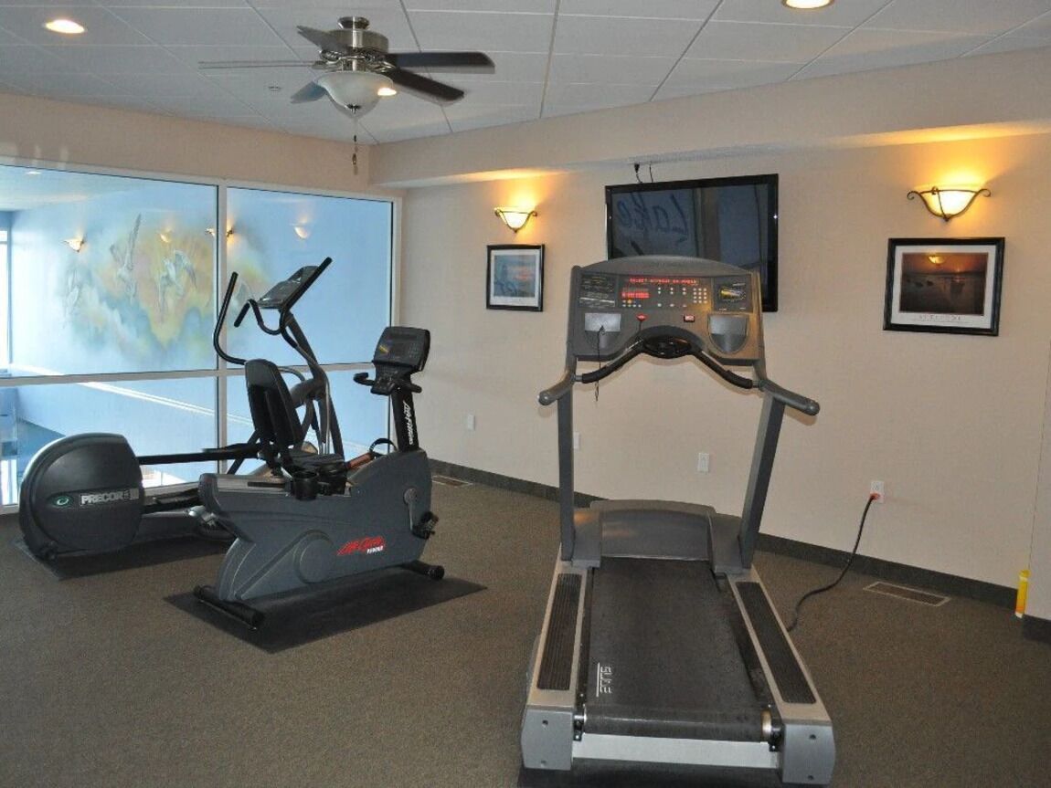 Ein Fitnessraum mit Cardiogeräten, darunter Laufbänder und ein Crosstrainer, großen Fenstern und Wandleuchten.
