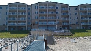 A multi-story residential building with balconies, a parking area, and a small dock-like structure. - BEACH LEVEL CONDO L08-2BR/2BA-Private Beach-Indoor Pool. (Geneva-on-the-lake)