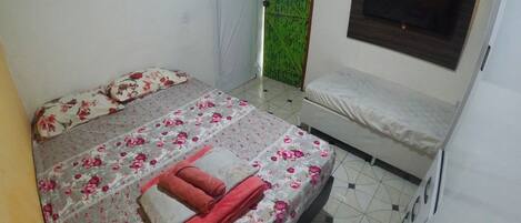 A bedroom with a bed, a bench, a TV, and a green door.
