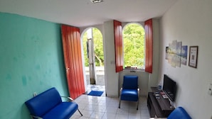 Une pièce avec deux chaises bleues, une petite table sur laquelle se trouve un téléviseur, et une fenêtre avec des volets rouges.