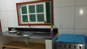 Une cuisine avec un évier, une fenêtre ornée de rideaux verts, une cuisinière et un tissu bleu sur le plan de travail.