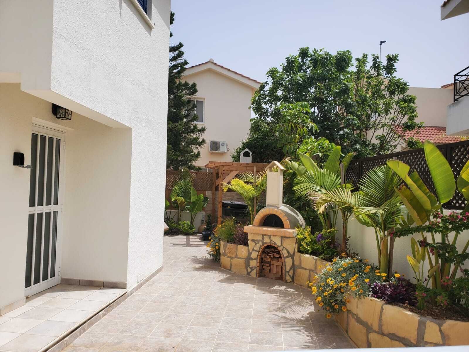 Un patio estrecho con un horno de piedra, plantas en macetas y una pérgola de madera.