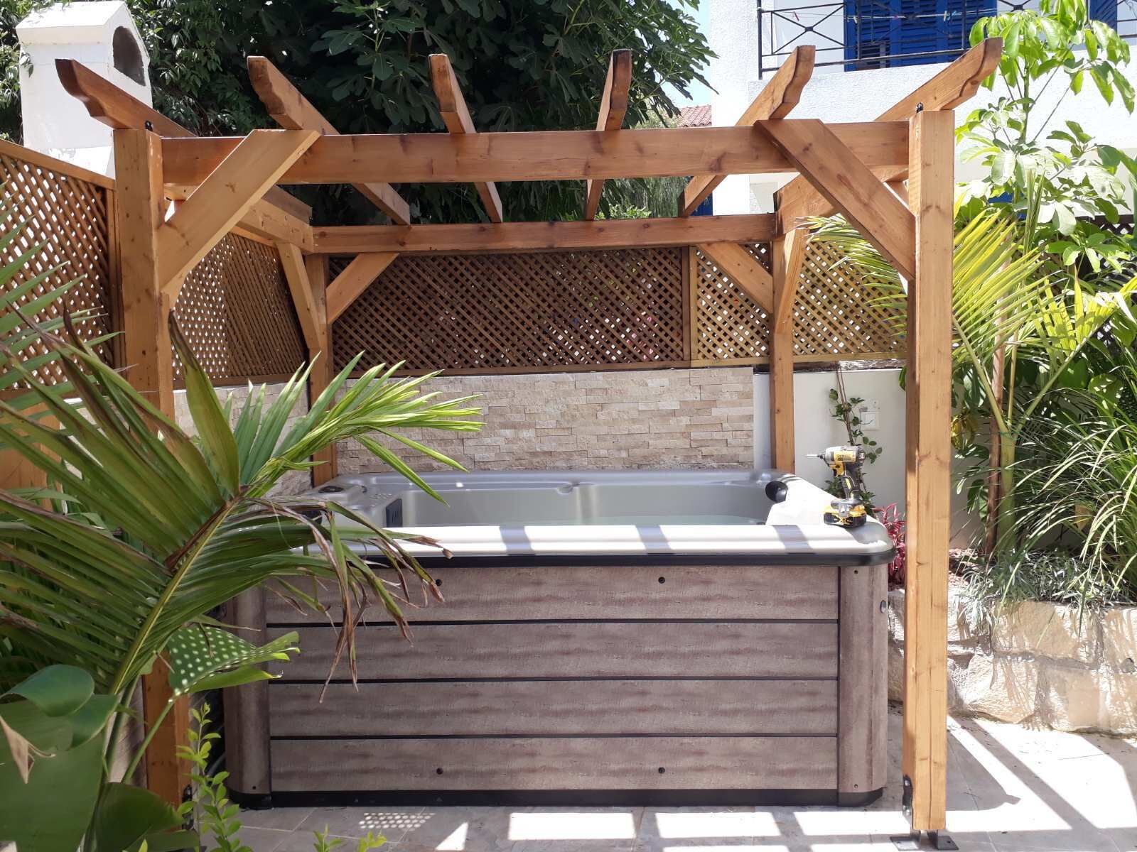 Un bain à remous sous une pergola en bois, avec un mur en briques en arrière-plan.