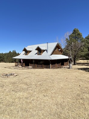 A log cabin with a metal roof, wooden deck, and a fire pit in the yard.