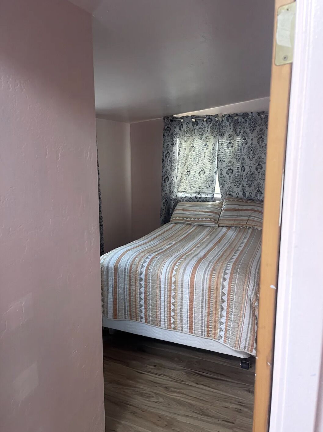 A bedroom with a bed, patterned curtains, and a wooden floor.